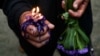 Un devoto sostiene una vela encendida en su mano y un ramo de flores moradas, en tributo a San Lázaro.