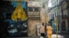 Cubanos en un área restrigida por casos de COVID-19, junto a una imagen de la Virgen de la Caridad. (YAMIL LAGE / AFP)
